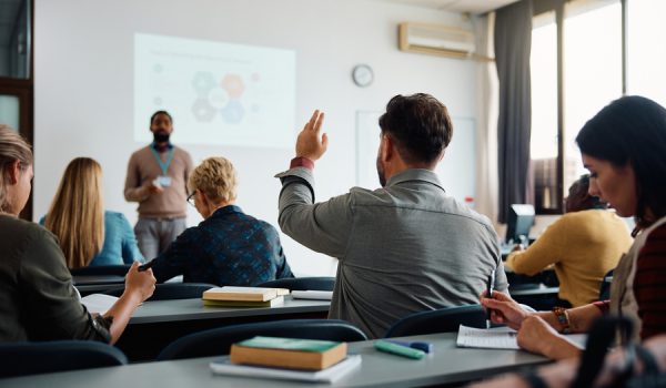 Rear view of man raising arm to ask a question during a presentation in lecture hall.