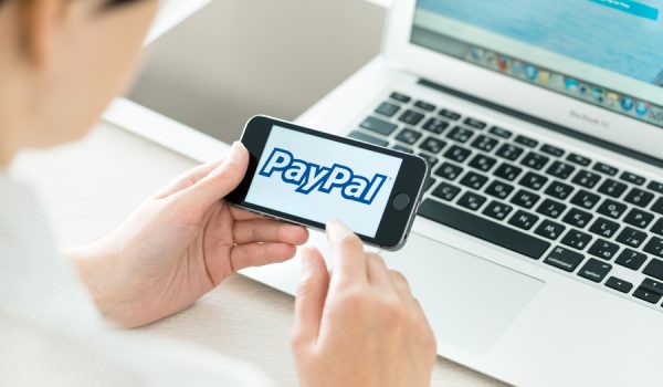 Kiev, Ukraine - June 27, 2014: Person at workplace holding in hand a brand new Apple iPhone 5S with PayPal logo on a screen. PayPal is the worldwide e-commerce business service allowing payments and money transfers via internet, founded in June, 1998.