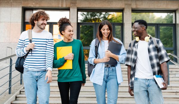 Happy students walking together on university campus, chatting and laughing outdoors after classes