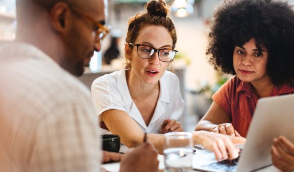 Business women having a work lunch in a café, exchanging ideas and discussing their projects with a client. Young business team using a laptop as they sit around a coffee table.