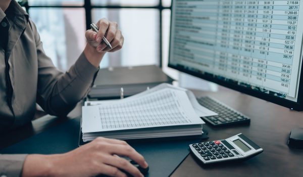 Investors working on desk office and check data cost, balance, profit and  currency on monitor screen. Accounting and  Financial concept.