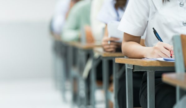Students Taking Exam in Classroom Setting. Students in uniforms are seated in a classroom, writing answers during an exam, highlighting focus and academic testing.