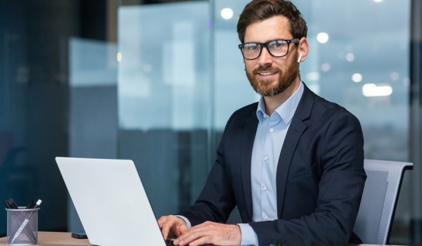 Portrait of mature successful and happy businessman, senior man with beard smiling and looking at camera, investor working with laptop inside office in business suit.