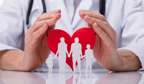 Close-up Of A Doctor's Hand Protecting Family Cut Out With Red Heart Shape